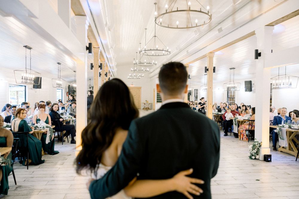 Wedding reception guests gathered in an elegant white venue with hanging chandeliers and modern decor.