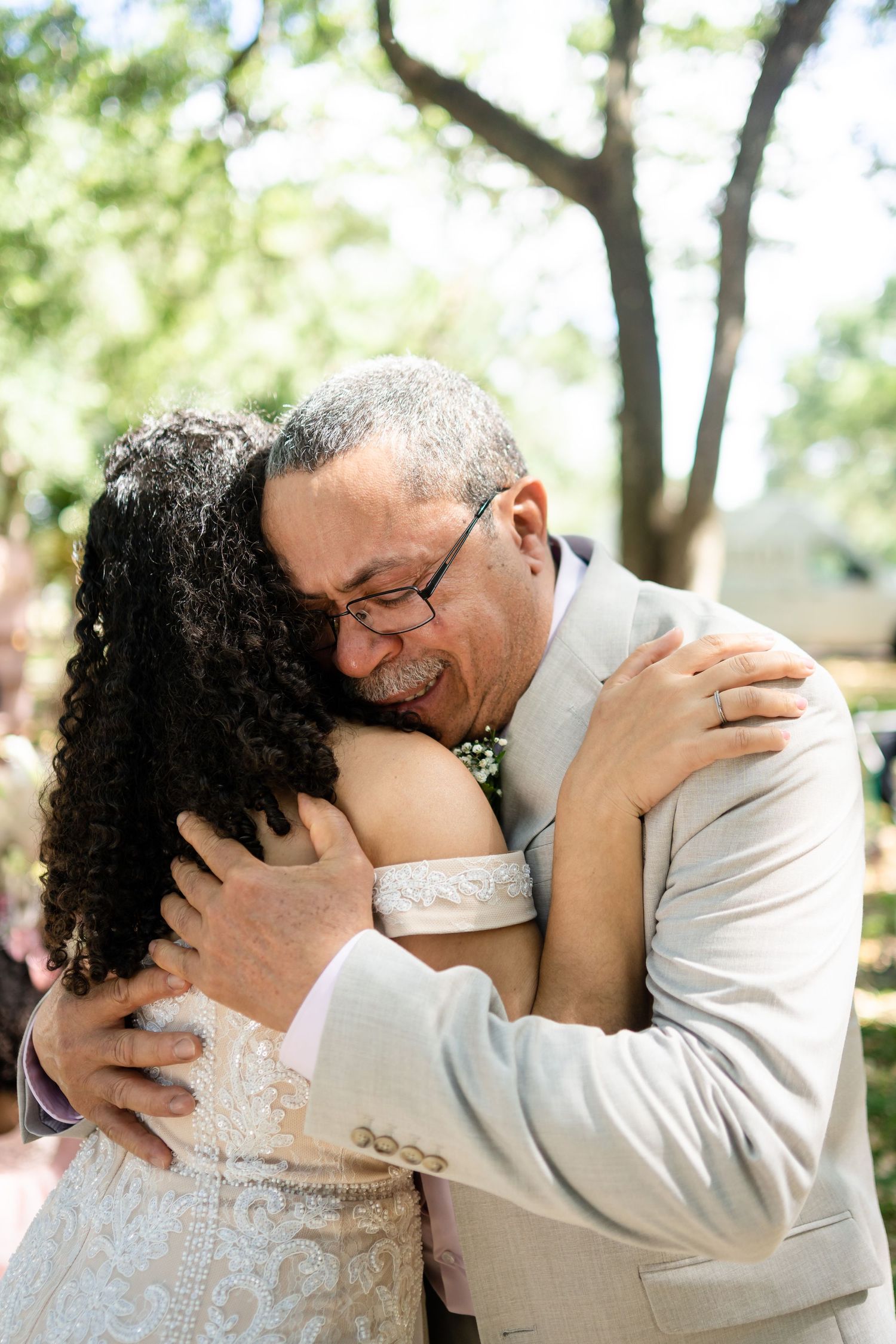 Emotional father-daughter embrace during wedding celebration outdoors.