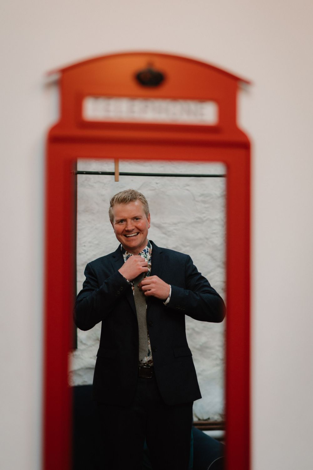 A person adjusts their tie while posing in front of a red British telephone box.