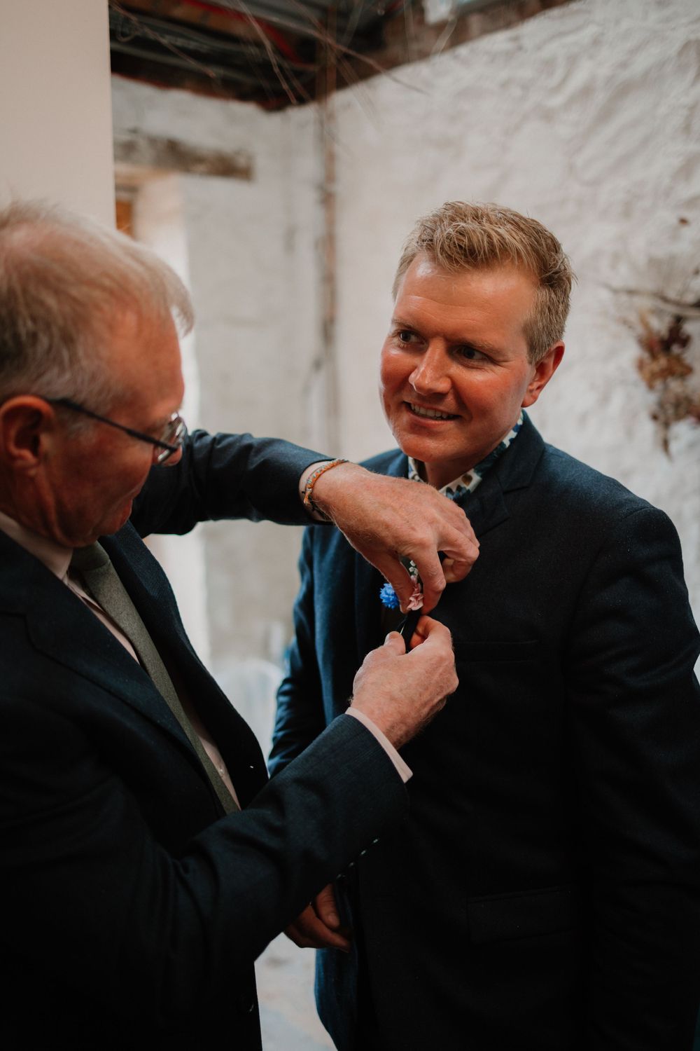 Two people share a candid moment while adjusting formal attire.