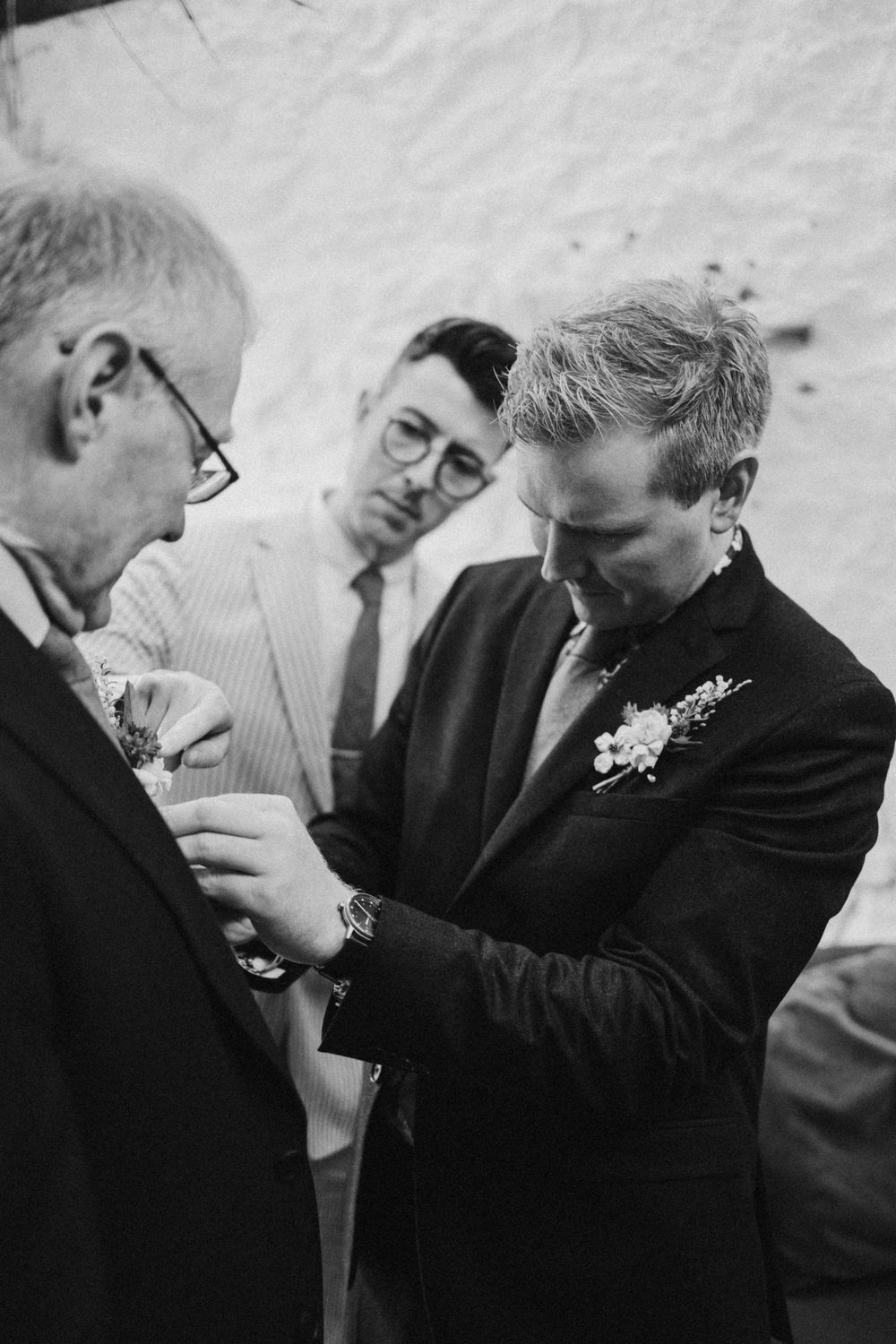 A black and white capture of three people during a formal attire preparation moment.