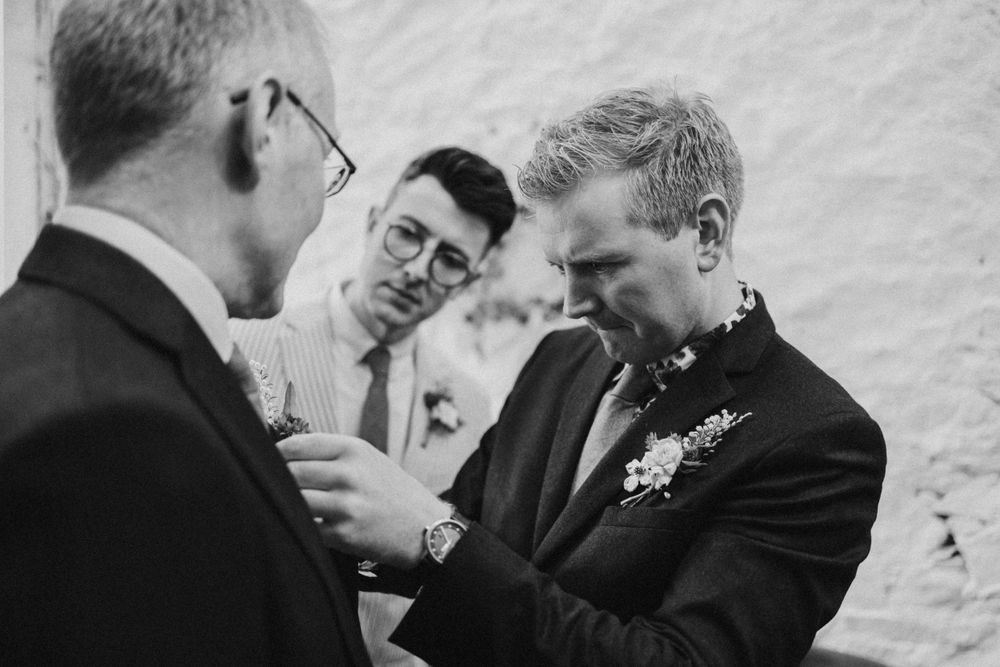 Three people in formal attire interact during a boutonniere pinning moment.