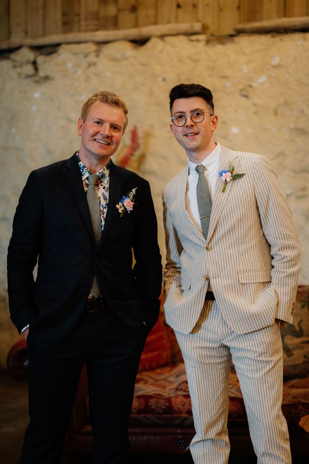 Two people in contrasting dark and light suits pose together at a wedding venue.