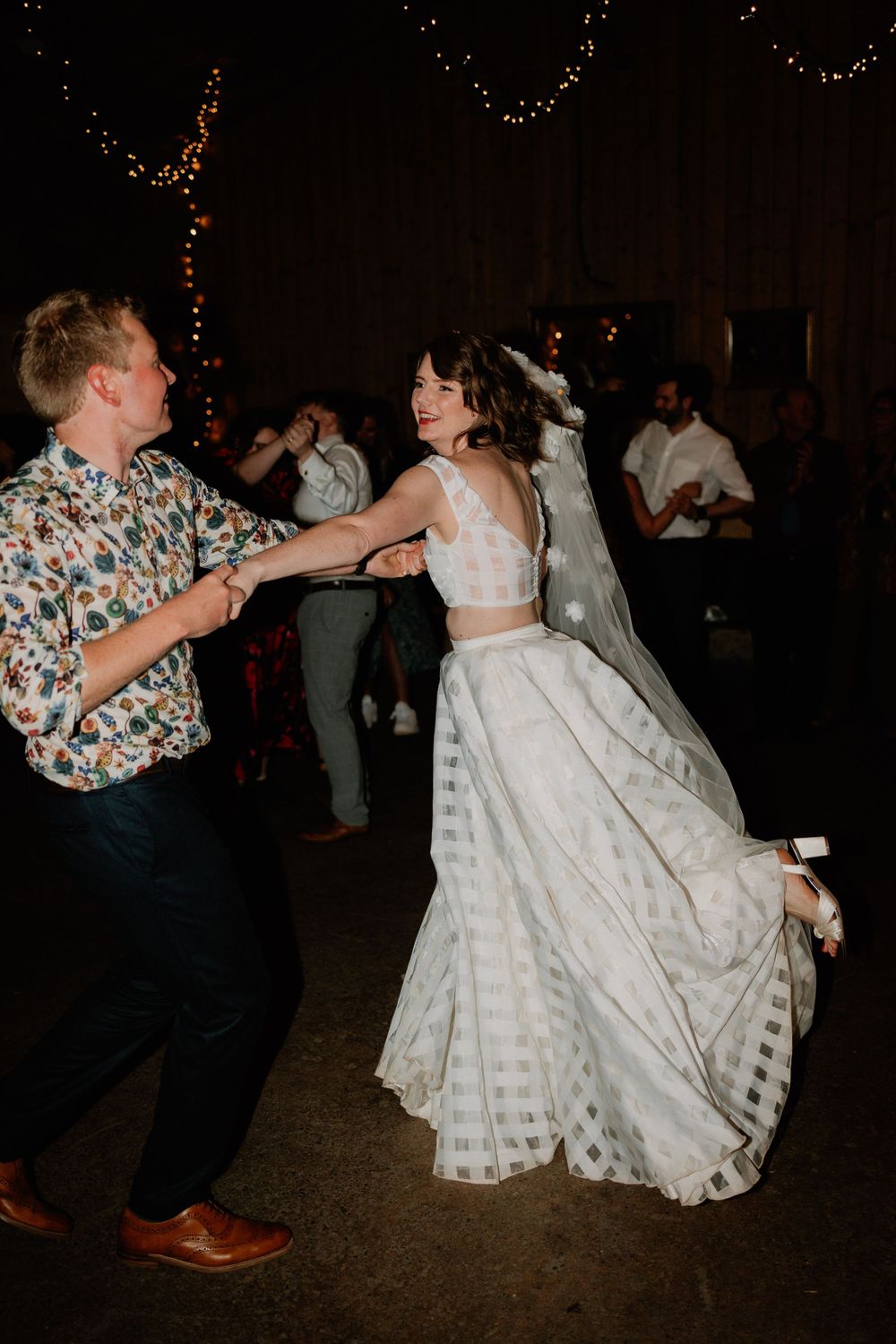 Dancing couple twirls on reception floor under ambient string lights creating dynamic movement.