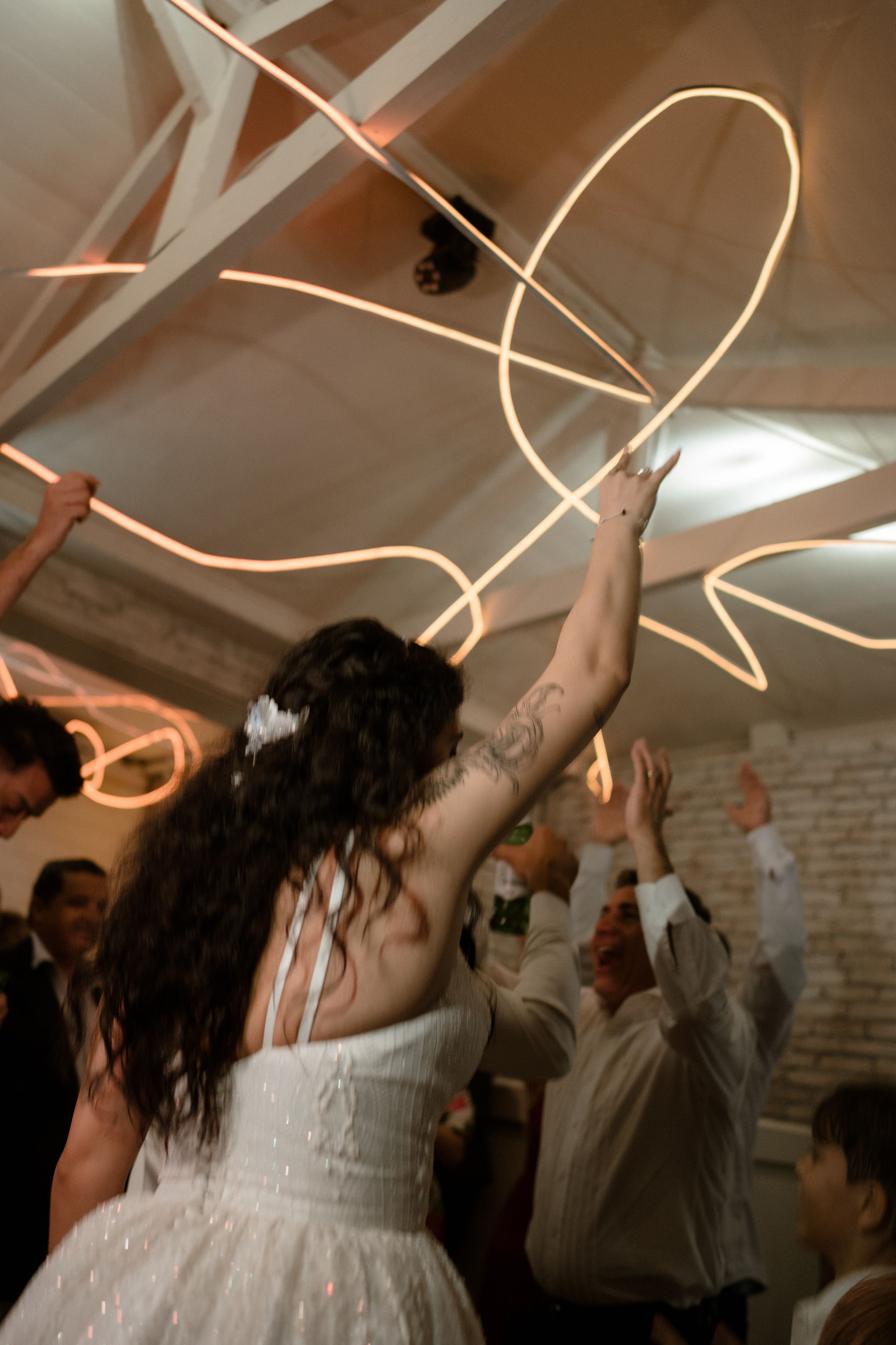 Wedding guests celebrating on the dance floor with swirling light trails in a brick-walled venue.