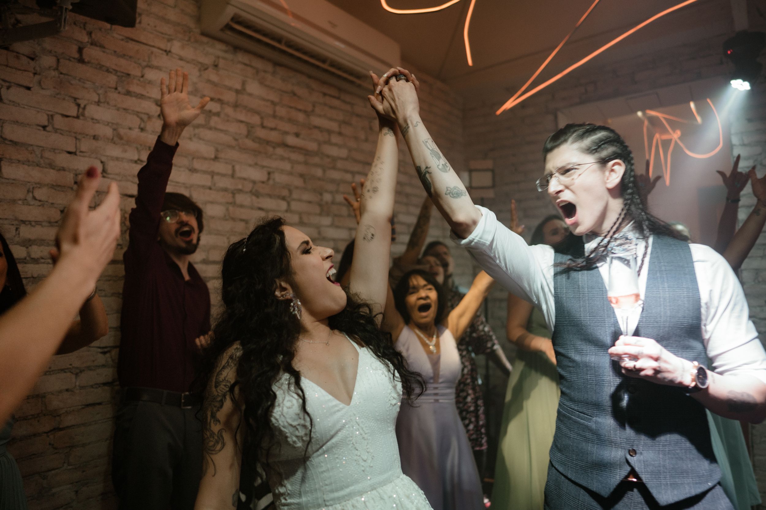 People dancing and celebrating at a wedding reception with decorative orange light trails visible above.