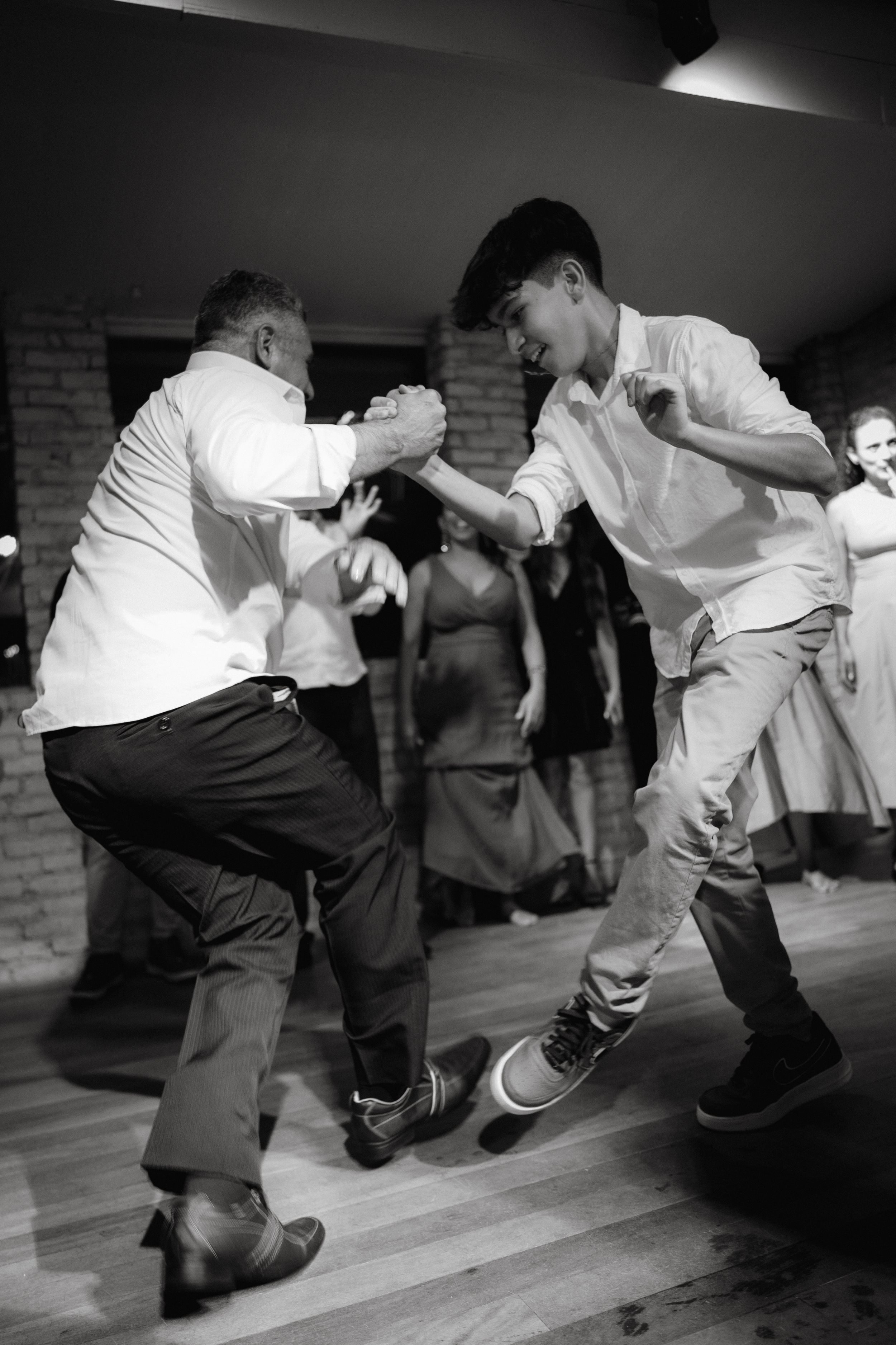 Two dancers performing energetic moves on a wooden dance floor in black and white.
