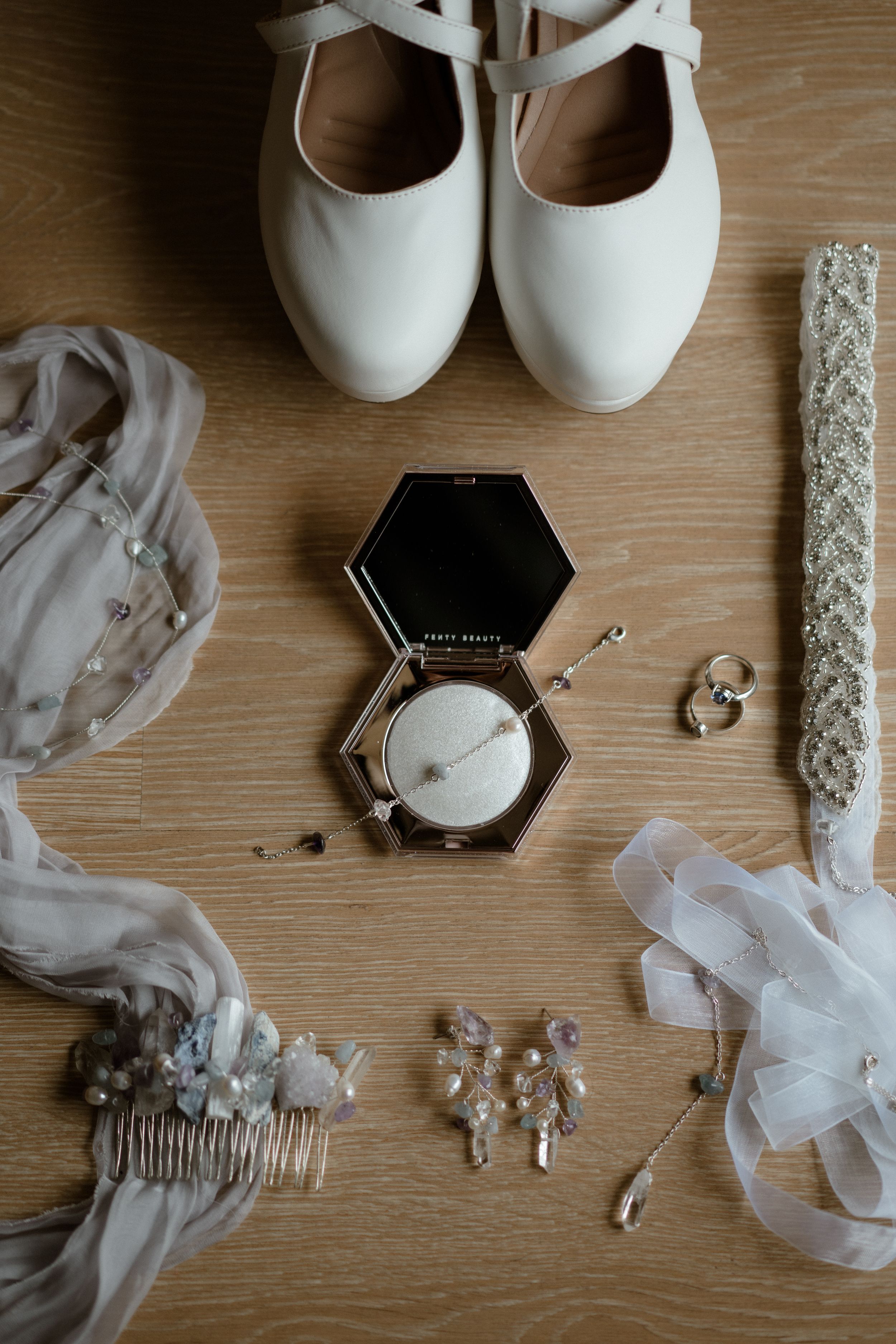 Wedding accessories including white shoes, jewelry, and a hair comb arranged on a wooden surface.
