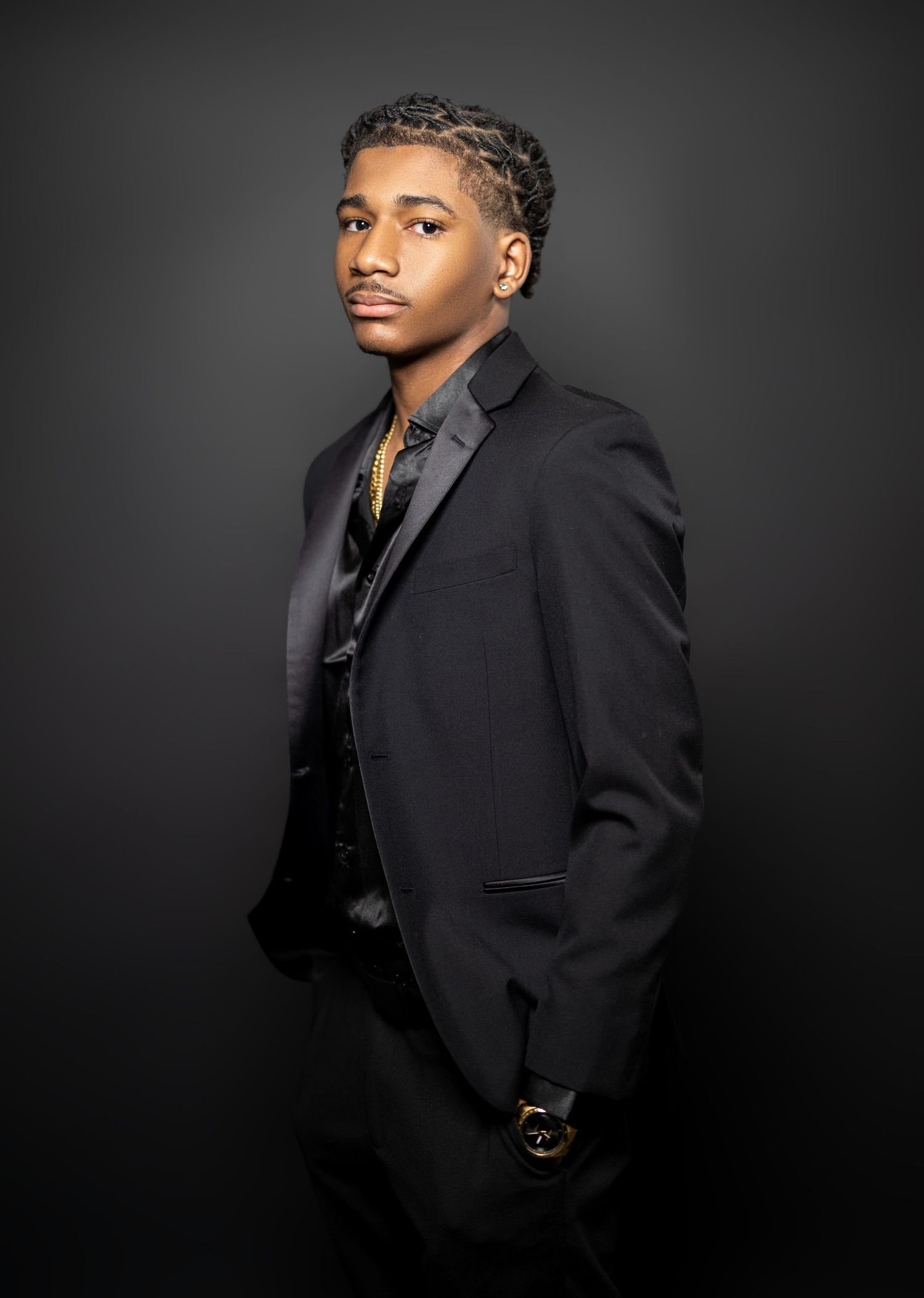Professional studio portrait of person in black suit against dark background.