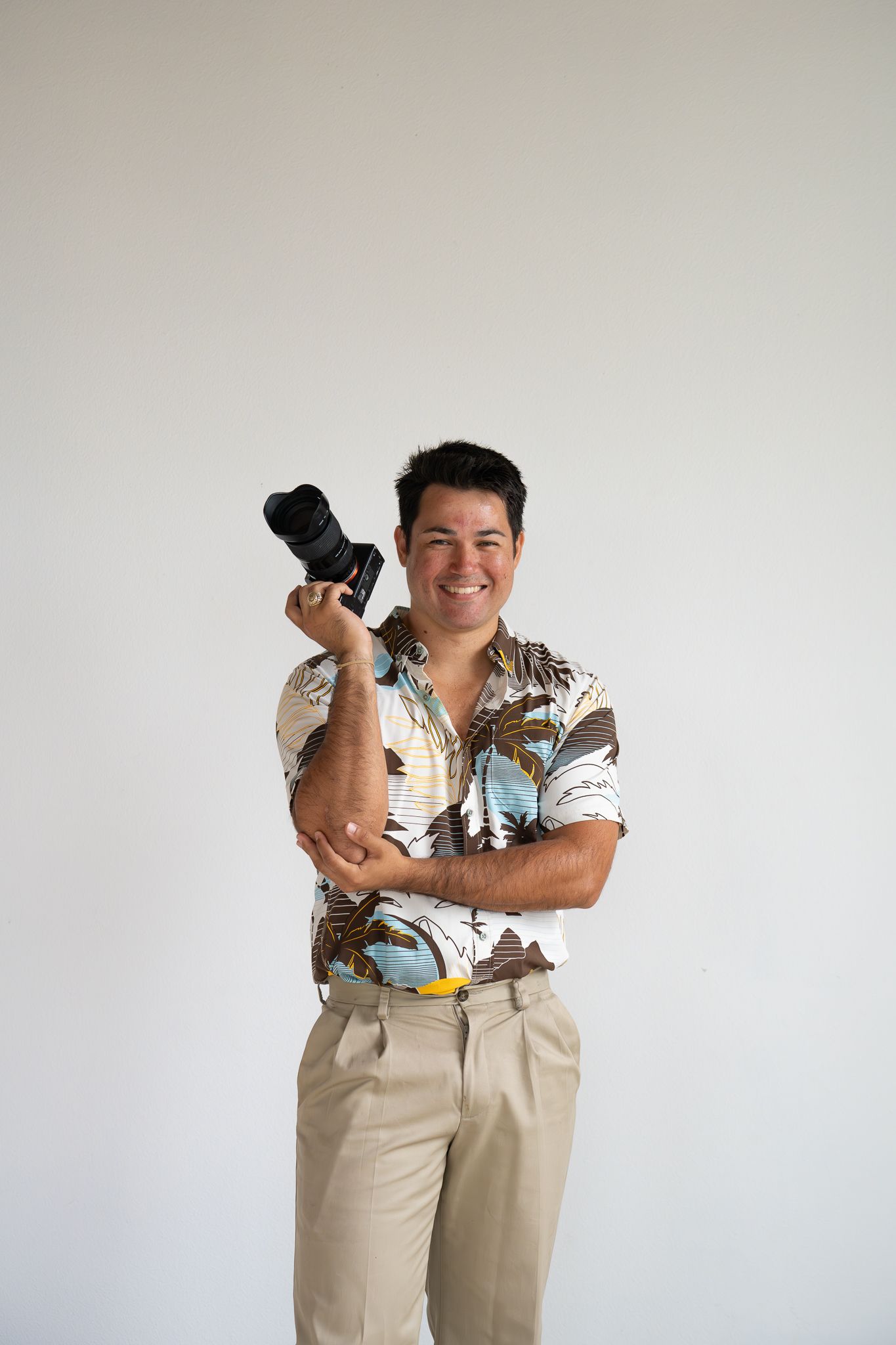 Person wearing a beige short-sleeve button down with tropical beach print standing in backyard by wooden fence.