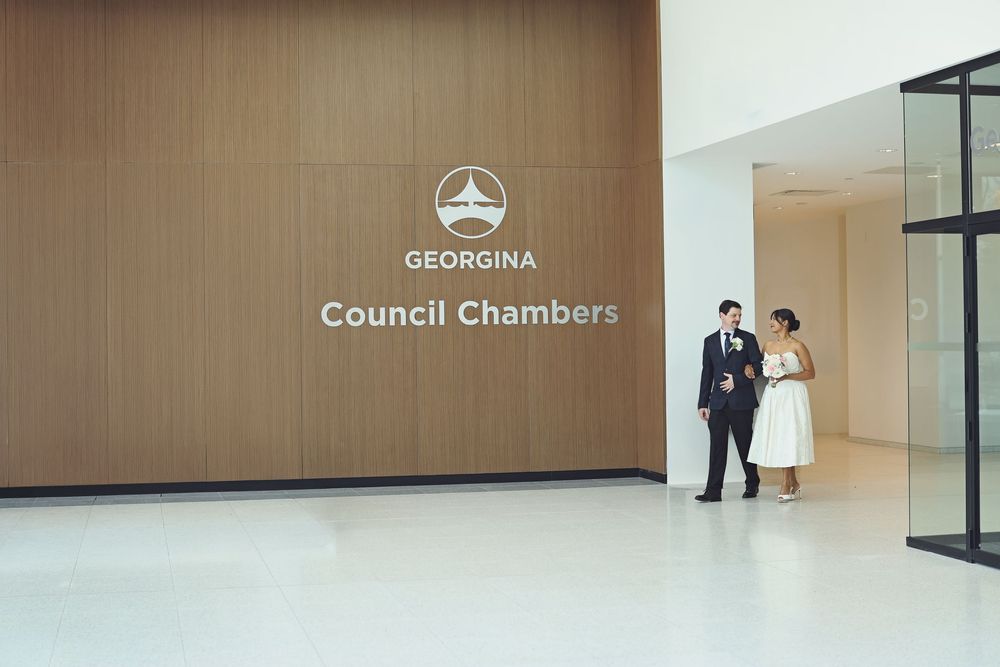 Couple posing in front of Georgina Council Chambers wooden wall in a modern building interior.