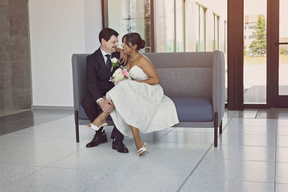 Bride and groom share a romantic moment seated on a gray sofa in a modern venue on their wedding day.