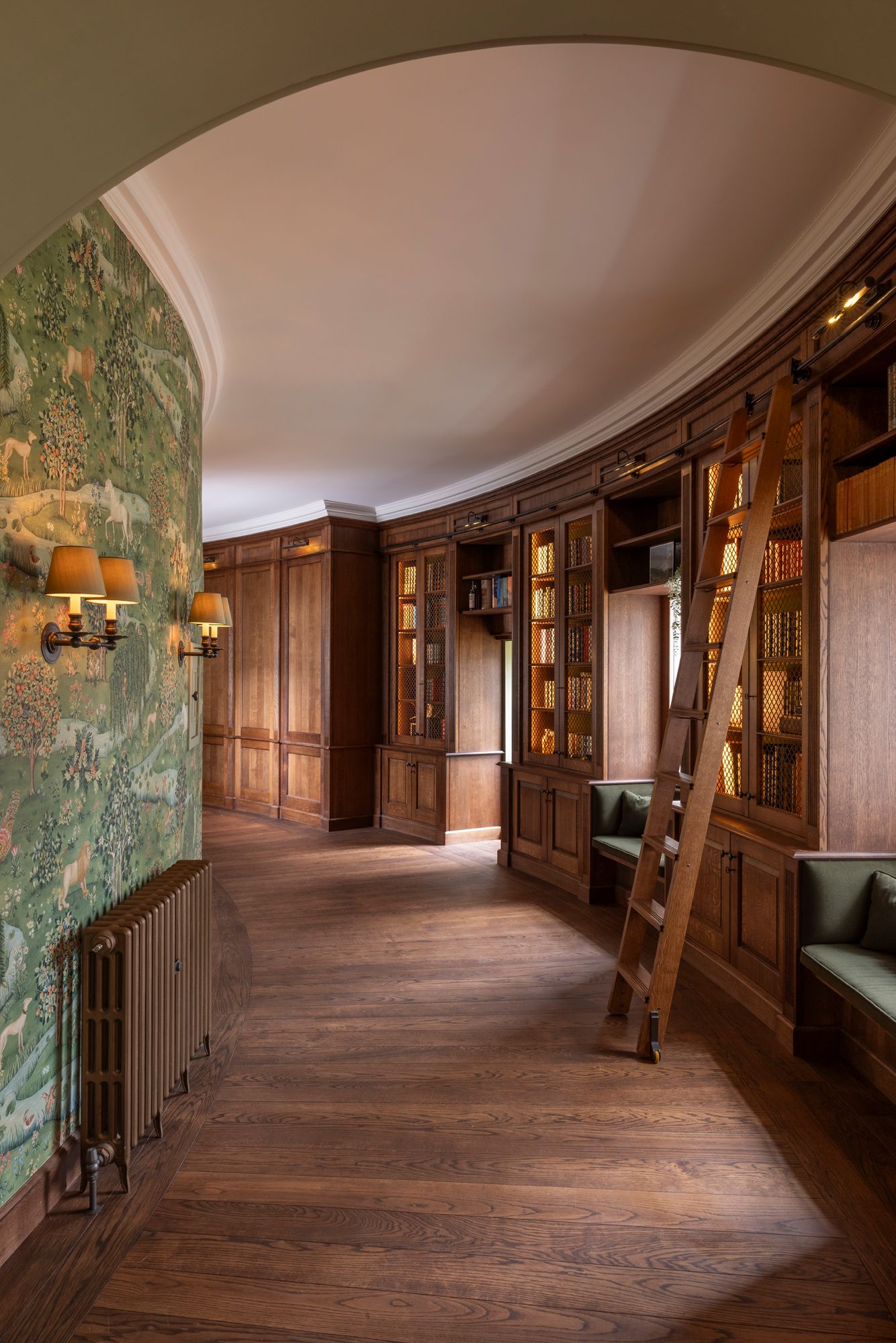 Curved hallway with antique wood paneling, hardwood floors, and vintage wall sconces in a historic building interior.