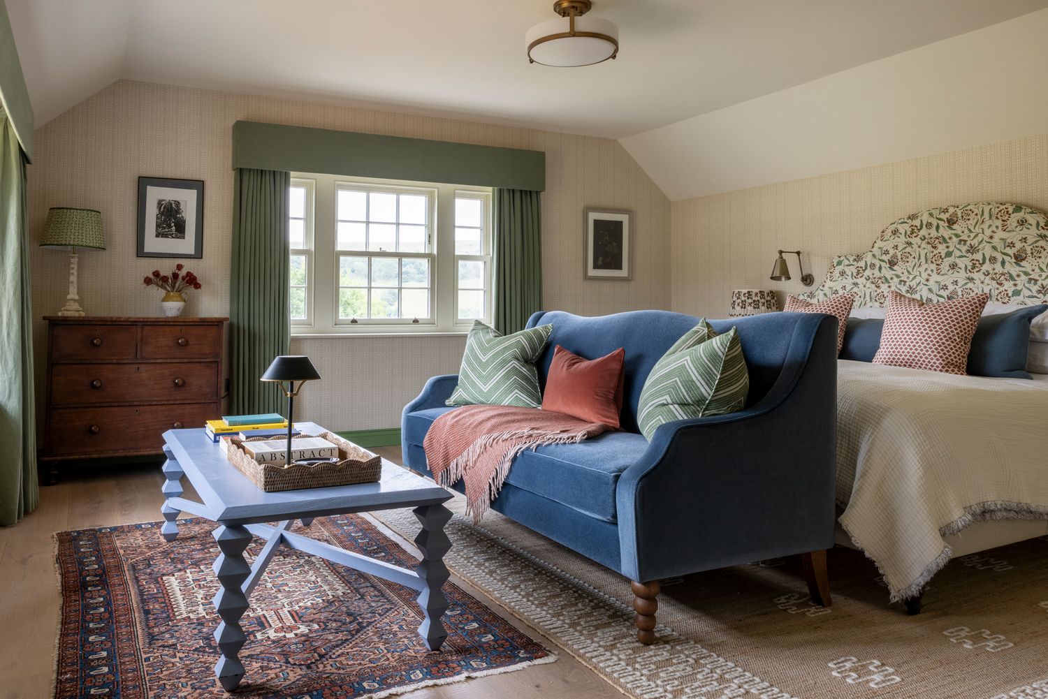 A panoramic view of a cozy bedroom with a blue sofa, pillows, and natural light streaming through windows.
