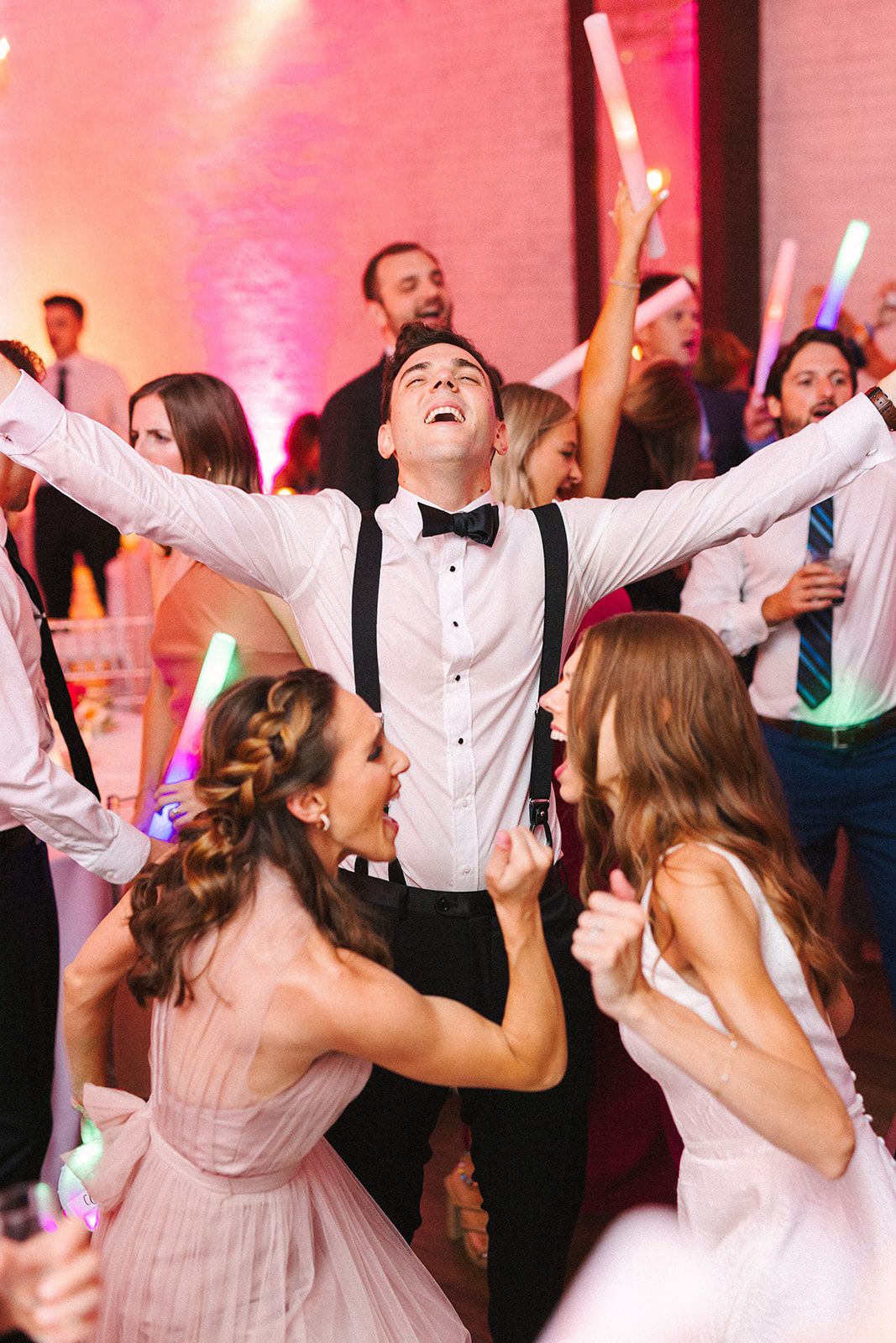 Wedding party guests dancing and celebrating enthusiastically on the dance floor with glow sticks and formal attire.