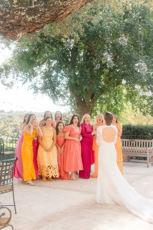 Bridesmaids in vibrant orange and red dresses pose with bride on a sunny terrace at San Antonio Country Club.