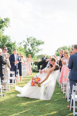 A celebratory wedding ceremony moment on a manicured lawn with white chairs and guests at the Dallas Arboretum's a Tasteful Place Lookout