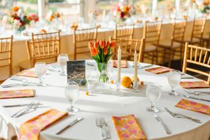 An elegant wedding reception table setting with orange accents and gold chiavari chairs at the Dallas Arboretum's a Tasteful Place
