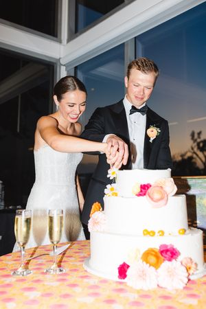 A couple cutting their elegant white wedding cake decorated with bright flowers and citrus at the Dallas Arboretum's a Tasteful Place