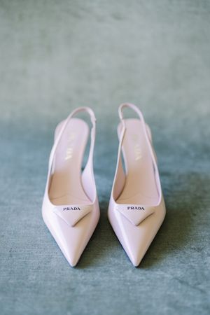 A pair of elegant pink Prada slingback heels with pointed toes positioned on a gray textured surface.