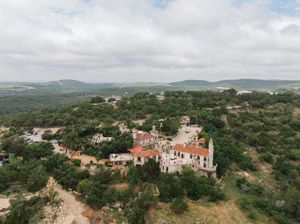 A panoramic aerial view of a Mediterranean coastal village nestled among rolling green hills and vegetation.