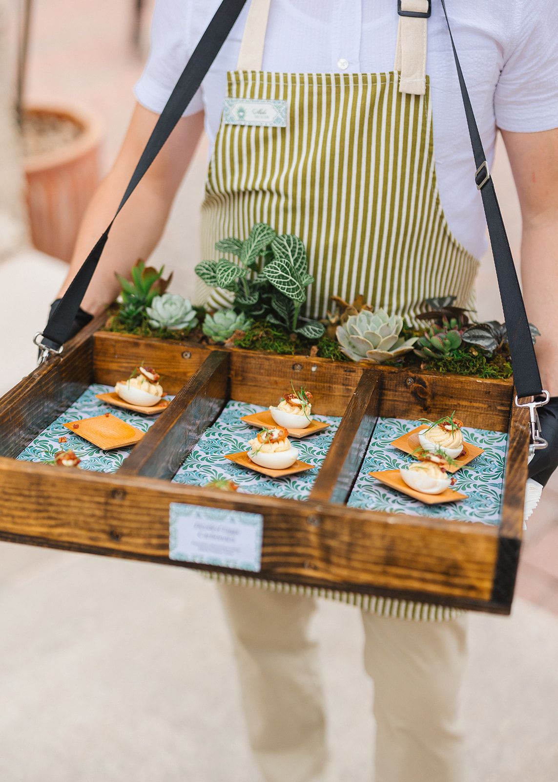 Wooden serving tray with three gourmet appetizers on blue patterned tiles decorated with succulents and greenery.