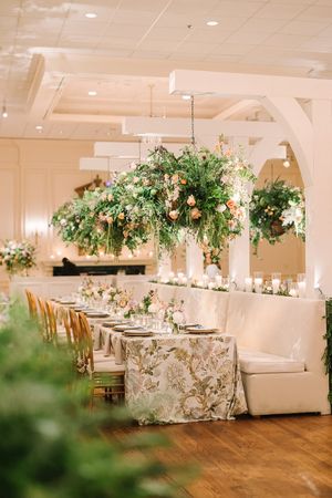 Elegant wedding reception venue with lush green floral centerpieces, floral tablecloths and white banquette seating.