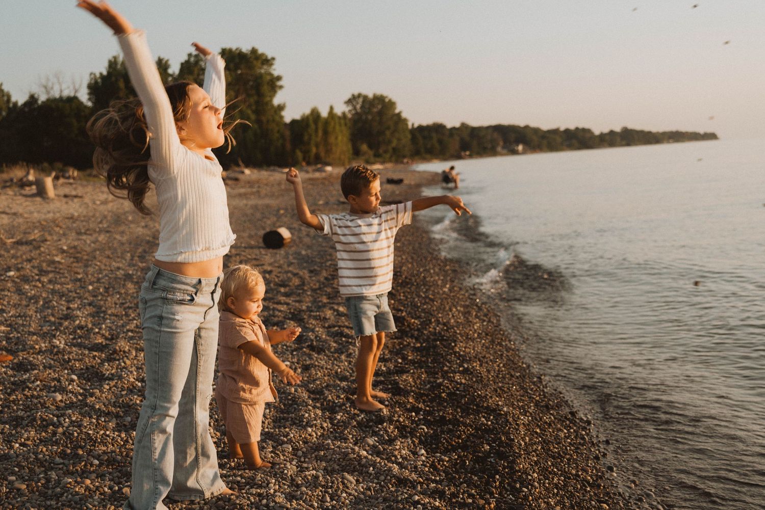 Family enjoying sunset at rocky beach shoreline with arms raised in celebration.