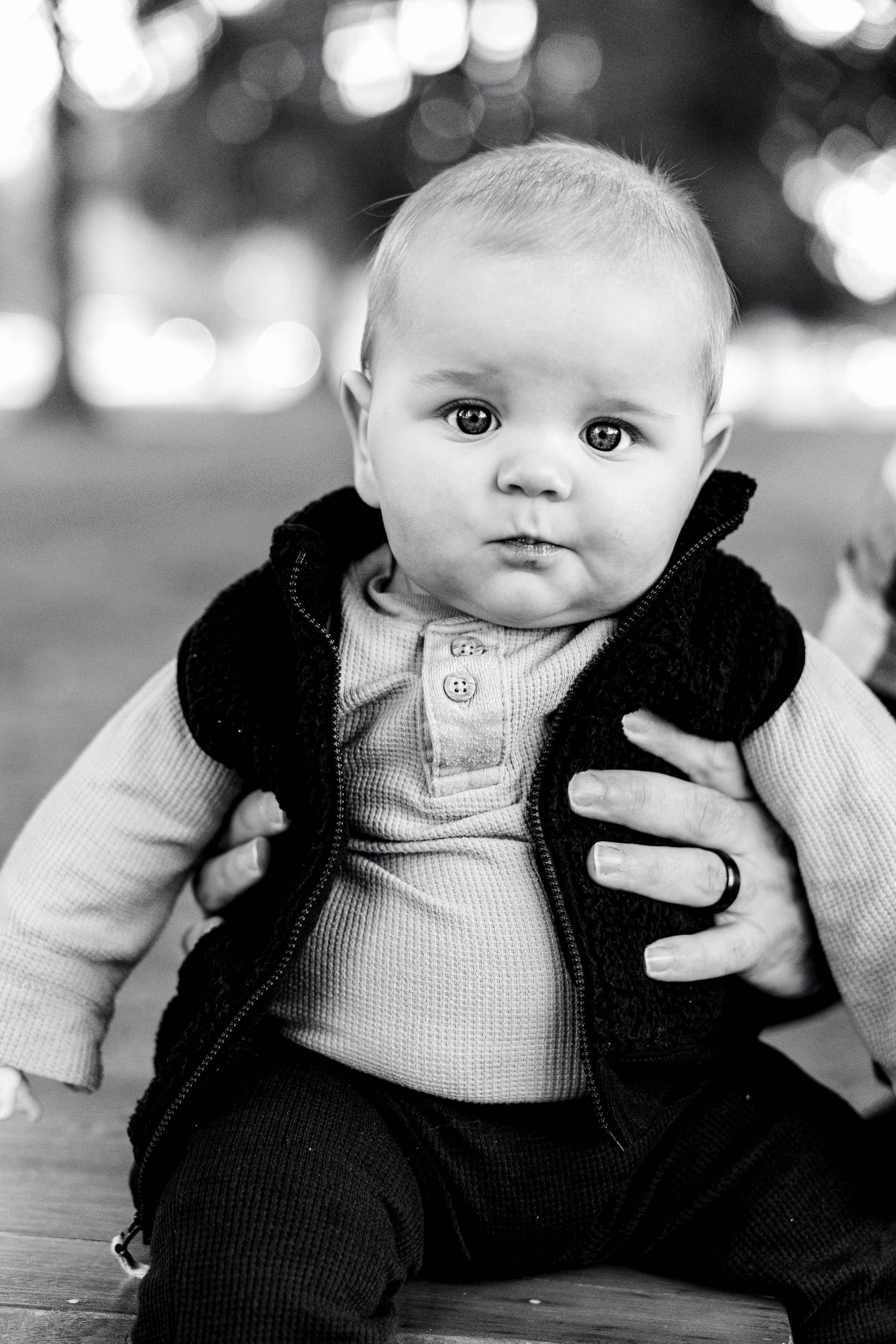 Baby wearing vest and ribbed outfit sitting with wide-eyed expression.