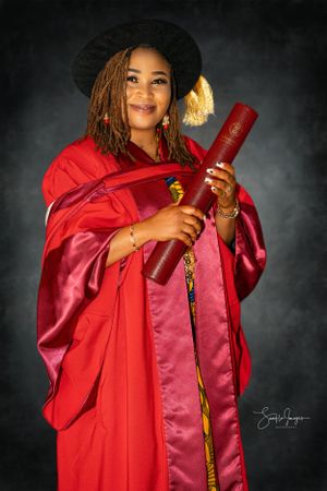 Graduate in red academic regalia and black hat holds diploma while smiling in professional graduation portrait.
