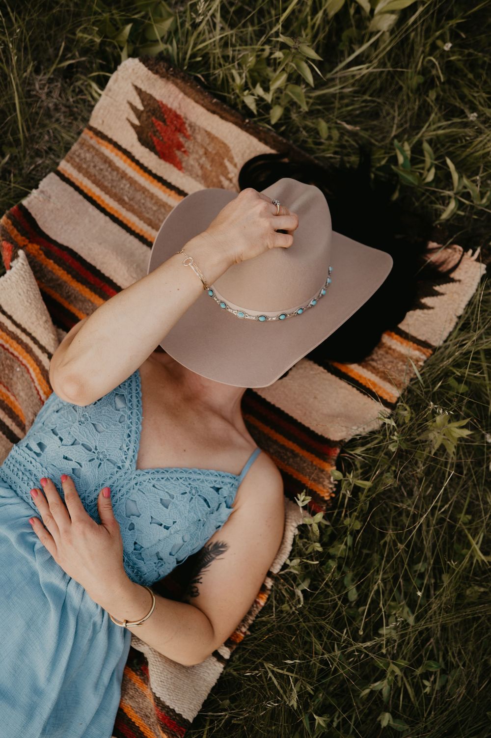 Person in a light blue summer dress reclines on wooden bench in a garden setting while basking in natural sunlight.
