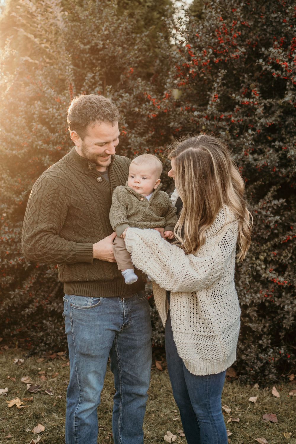 A couple wearing cozy sweaters shares a tender moment outdoors with their baby on an autumn evening.