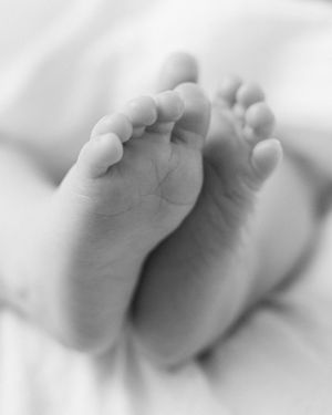 Close-up black and white photo of tiny newborn baby feet resting on a soft white blanket.