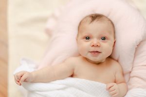 Adorable newborn baby wrapped in a soft white towel, lying on a pink blanket with a sweet smile.