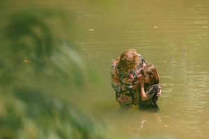 Two people sharing an intimate moment while standing in a calm green lake surrounded by lush foliage.