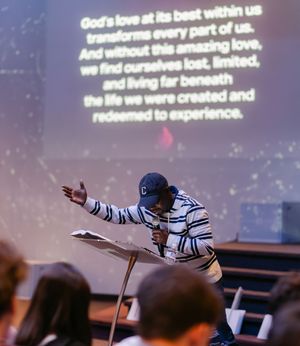 Pastor preaching passionately at church pulpit with projected sermon text about God's love visible on screen behind him.