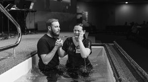 A man and woman stand in a baptismal pool during a Christian baptism ceremony in a church.