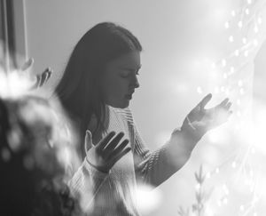 Black and white photo of a woman in a sweater reaching toward a bright glowing light source.
