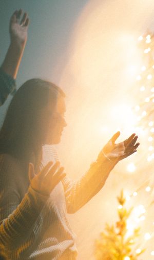 Woman with raised hands basking in golden light during worship and prayer.