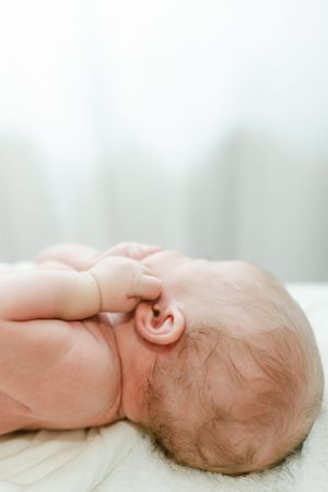 Close-up of a sleeping newborn baby lying on its side, with tiny hand near ear and fine hair visible.