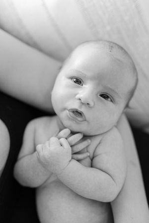 Black and white portrait of a newborn baby with hands clasped, looking up with wide curious eyes.
