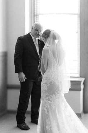 Black and white wedding photo of bride in lace gown and veil with groom in suit sharing an intimate moment.