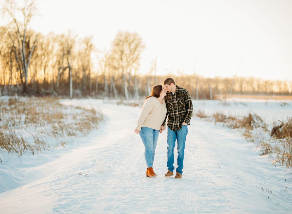 Couple walking together on a snowy path during winter sunset.
