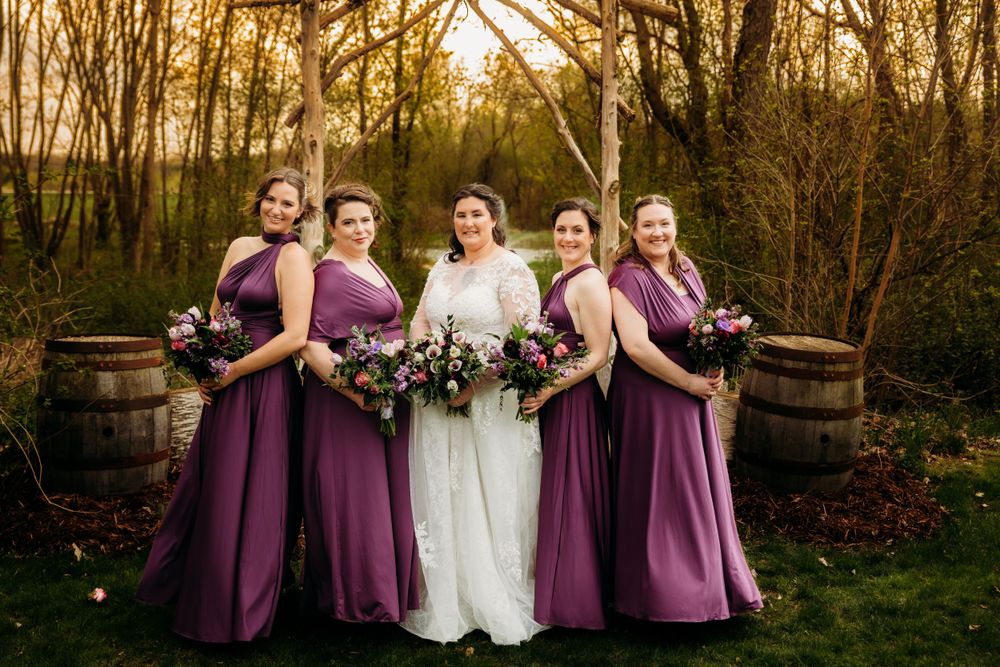 Wedding party in purple dresses posing in garden setting at sunset.