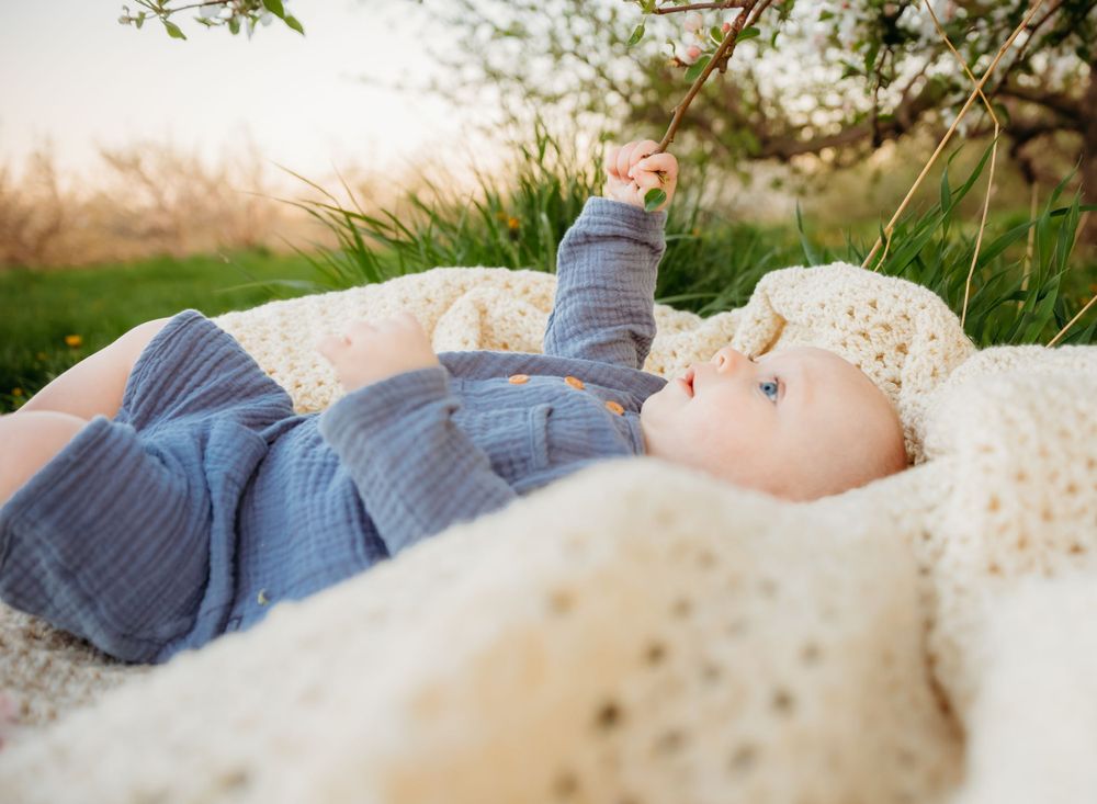 Baby lying on a cream blanket outdoors reaching toward the sky at sunset.