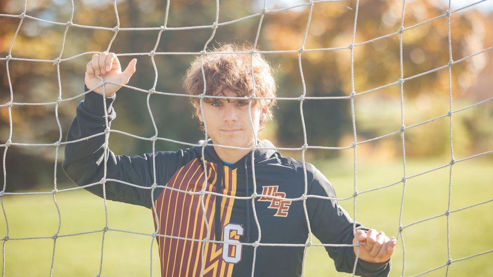 Athlete holding rose while standing in front of soccer goal net during golden hour.