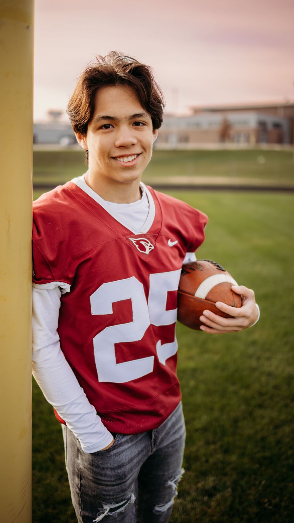 Football player in red jersey number 25 holding ball on field at sunset.