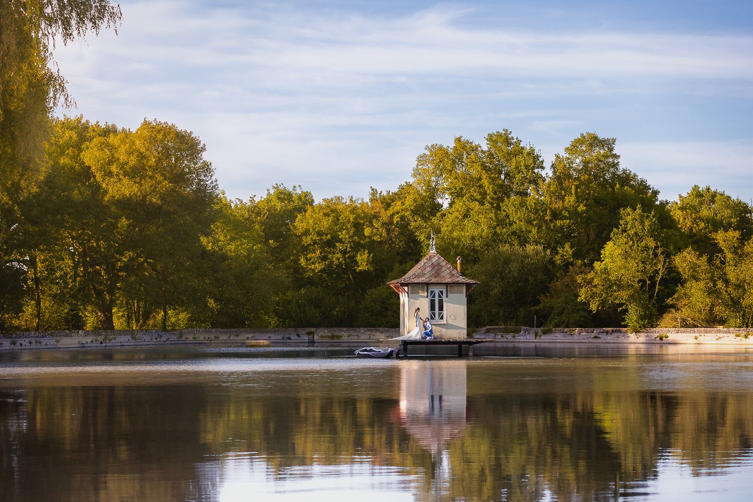 Serene lake view with white gazebo reflecting in calm waters during golden hour.
