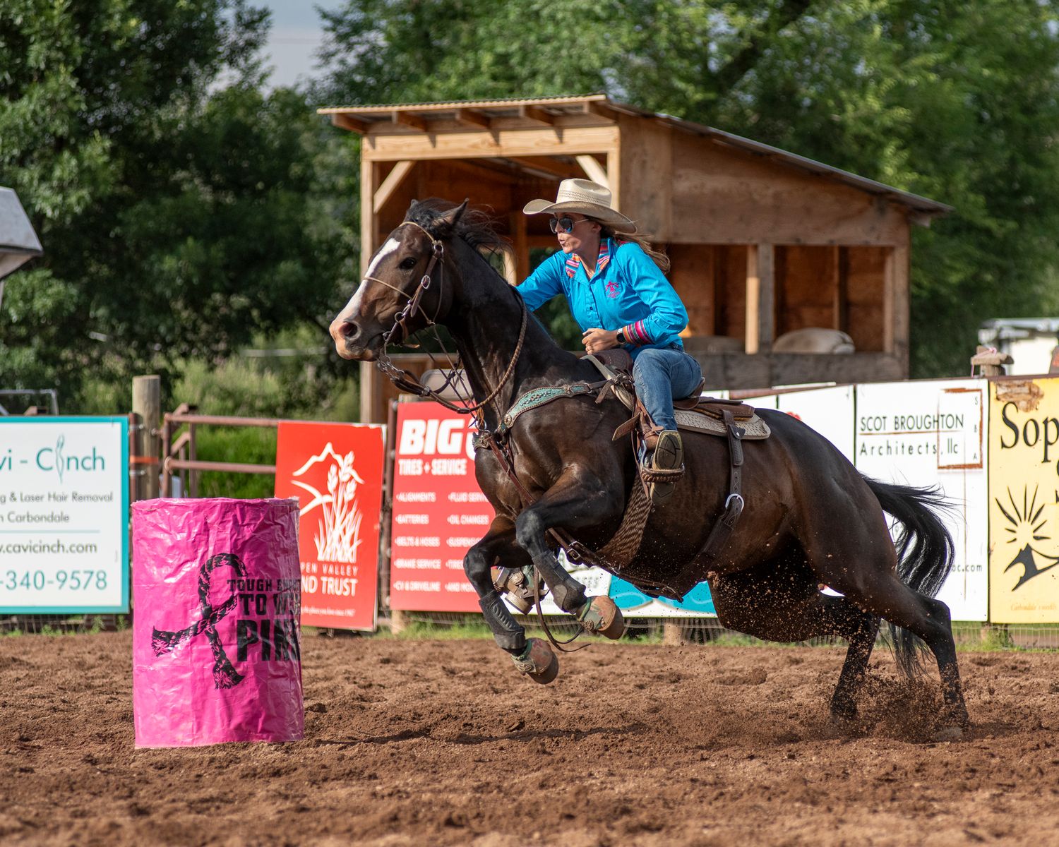 A competitive barrel racer rounds a pink barrel in an outdoor arena during a rodeo event.