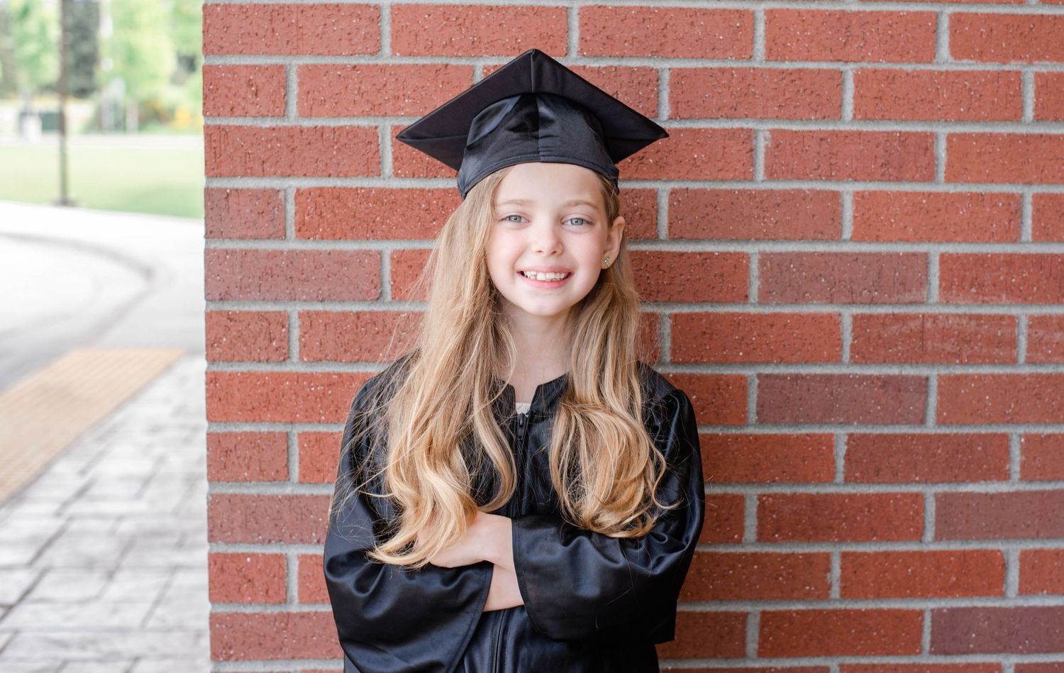 Graduate in traditional black academic regalia poses for portraits against brick wall backdrop.
